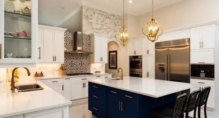 Palmhouse kitchen with white cabinets, a navy island with black stools, brass pendants and a patterned tile backsplash