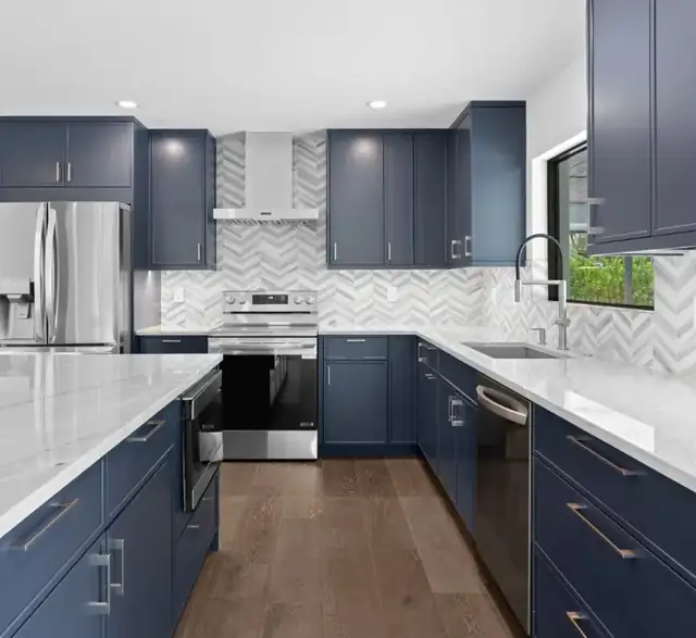 Navy shaker kitchen with white quartz counters, herringbone tile backsplash and wide-plank wood floor
